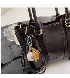 Detail of a baseball charm with mini bat and ball on a brown leather tote handbag