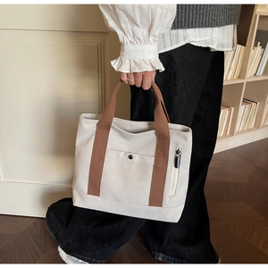 Close-up of canvas tote bag with brown straps and functional metal snap button pocket