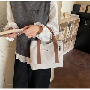 Detailed close-up of cream canvas tote bag with brown straps and secure metal snap pocket