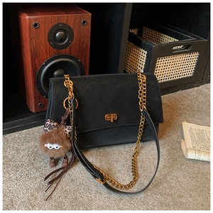 Detail of black matte leather crossbody bag with gold twist lock and plush bear charm