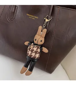 Close-up of a cute rabbit doll charm with houndstooth vest hanging on a brown tote bag
