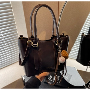 Close-up of deep brown tote bag with gold logo, baseball charm, and top handles