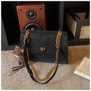 Detail of black matte tote with golden chain strap and cute brown plush charm accessory