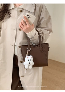 Detail of dark brown lychee pattern leather handbag with a cute plush dog pendant charm