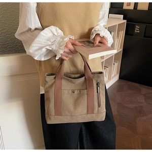 Detailed close-up of khaki canvas tote bag featuring brown woven handles and metal snap button