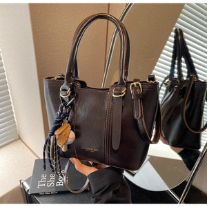Detail of vintage brown bucket bag with smooth leather texture and sports-themed keychain