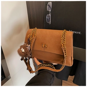 Detail of brown leather bag with gold chain strap, twist lock and plush monster charm