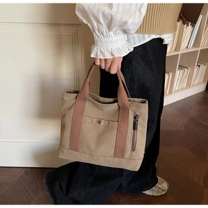 Detail of khaki canvas tote bag showing side zipper pocket and red handles in a library