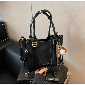 Detail of black glossy bucket bag featuring gold hardware and a baseball charm detail