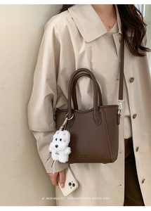 Detail of dark brown lychee leather bucket bag with cute white plush dog charm
