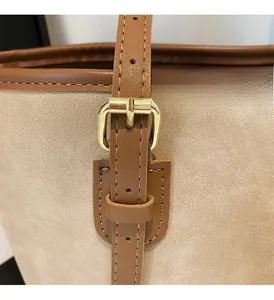 Close-up of golden metal buckle and MIKA logo on beige suede shoulder bag