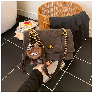 Detail of dark grey faux suede shoulder bag featuring a gold clasp and fuzzy monster charm