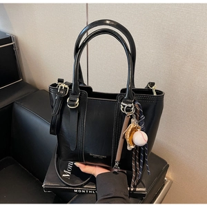 Detail of black glossy handbag with baseball charm and detachable shoulder strap