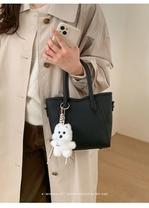 Detail of black pebbled leather bucket bag with cute white plush dog charm on handle