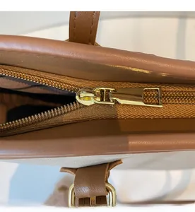 Close-up of smooth gold-tone zipper and textured brown leather on tote bag