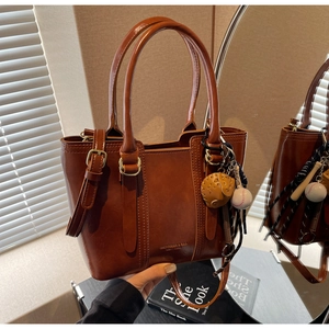 Detail of a brown glossy leather bucket bag with sports charms and adjustable strap