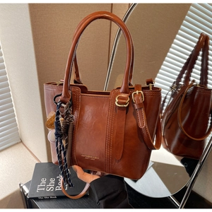 Detail of a brown leather tote bag with gold lettering and retro woven charm