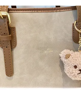 Close-up of beige suede tote bag with brown leather trim and a pink teddy bear charm