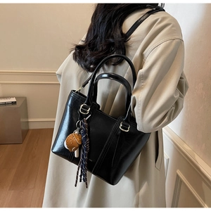 Detail of a black crossbody bucket bag featuring a decorative ribbon and a bear charm pendant