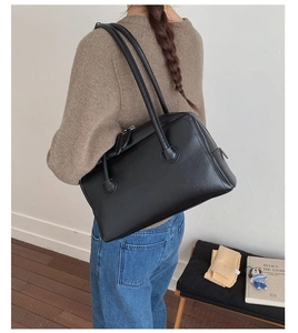 Minimalist black leather Boston bag worn as a shoulder bag in a lifestyle setting