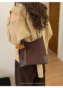 Détail du sac à bandoulière en daim marron foncé avec breloque ours et pompon rayé