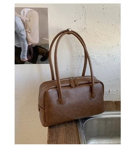 Detailed close-up of brown leather shoulder bag with dual zippers and long handles