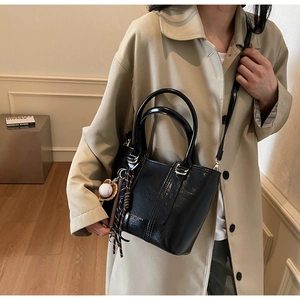 Detailed view of black polished crossbody bucket bag with decorative baseball charm and strap