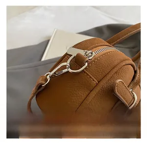Detail shot of silver metal hooks and zipper hardware on a brown leather round bag