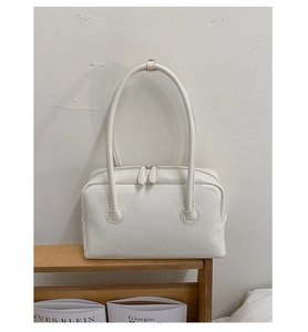 Detailed close-up of white leather Boston bag with dual zippers on a wooden shelf