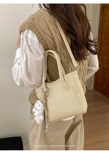 Detail of beige lychee grain leather bucket bag with plush charm and embossed logo