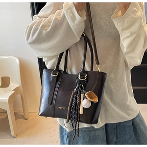 Detail of dark brown leather bucket bag featuring a vintage baseball charm and gold logo