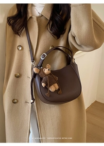 Detail of dark brown leather half-moon bucket bag with a cute bear charm pendant