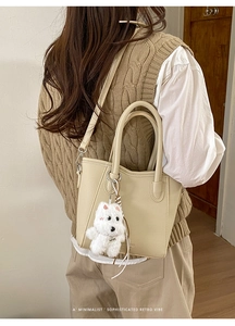 Detail of beige lychee grain bucket bag with a cute plush dog charm on crossbody strap