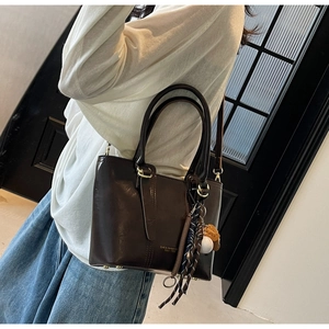 Detail of dark brown leather tote bag with baseball pendant and adjustable strap