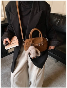 Brown leather bowling bag with silver buckle and rabbit fur charm shown on model