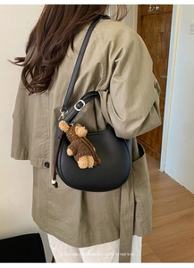 Detailed side view of a black lychee leather crescent bag with a cute brown bear charm