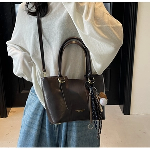 Detail of dark brown leather handbag featuring a baseball glove charm and gold text logo