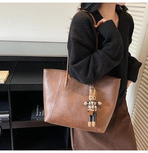 Detail of a brown leather tote bag featuring a gold logo and a cute rabbit charm