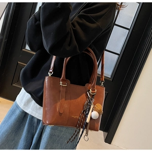 Close-up of caramel leather bucket bag featuring vertical stitching and sports charm detail