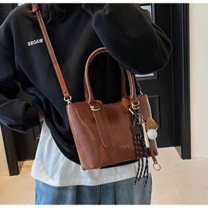 Detail of brown glossy PU leather tote bag with unique heart pendant and woven charms