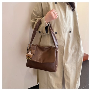 Detail of dark brown oil wax leather tote bag with metallic eyelets and bear charm