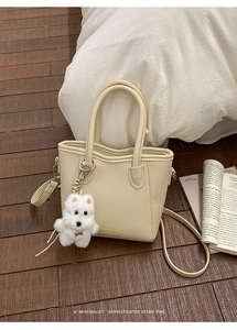 Close-up of off-white lychee leather tote with a cute plush dog charm on wood floor