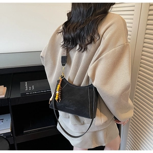 Detalle de bolso de hombro en ante negro con borla de cuentas y texto de moda