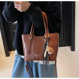Detail view of brown vintage PU leather bucket bag with logo and creative charm accessory