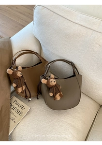 Detail of half-moon leather bags with plush bear charms on a cozy fabric sofa