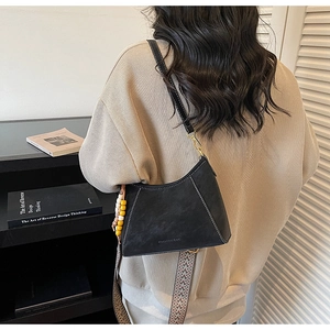 Detalle del bolso hobo de cuero mate negro con correa étnica y abalorios en una modelo