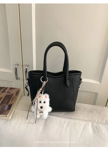 Detail of black lychee grain bucket bag with a cute white plush puppy charm and round handles