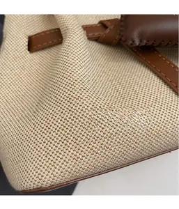 Close-up showing textured off-white canvas fabric and brown leather piping of the bucket bag