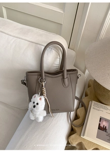 Detail of taupe pebbled leather bucket bag with dog charm on a white sofa
