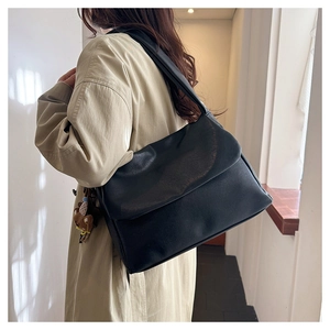 Side view of a large black oil wax leather tote bag worn with a stylish trench coat